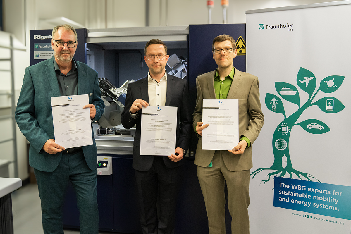 Dr. Michael Hippler, Managing Director of Rigaku Europe SE, Dr. Christian Reimann and Dr. Christian Kranert from Fraunhofer IISB with their award certificate in front of the Rigaku XRTmicron tool at the Center of Expertise for X-ray Topography at the IISB.