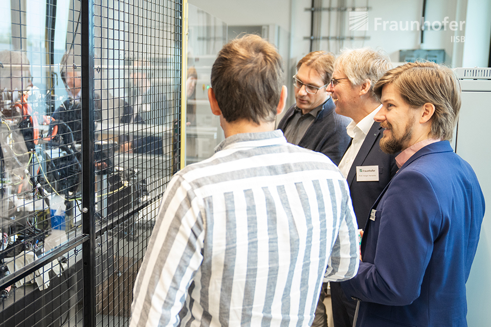 Doktorand Markus Meindl (links) präsentiert Prof. Hanselka das ausgebaute Wasserstoffsystems eines Brennstoffzellenfahrzeugs, was für detaillierte Untersuchungen im Wasserstofflabor des IISB aufgebaut wurde.